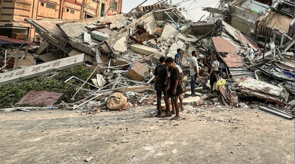 People stand past the debris of a collapsed building in Mandalay Myanmar after the earthquake