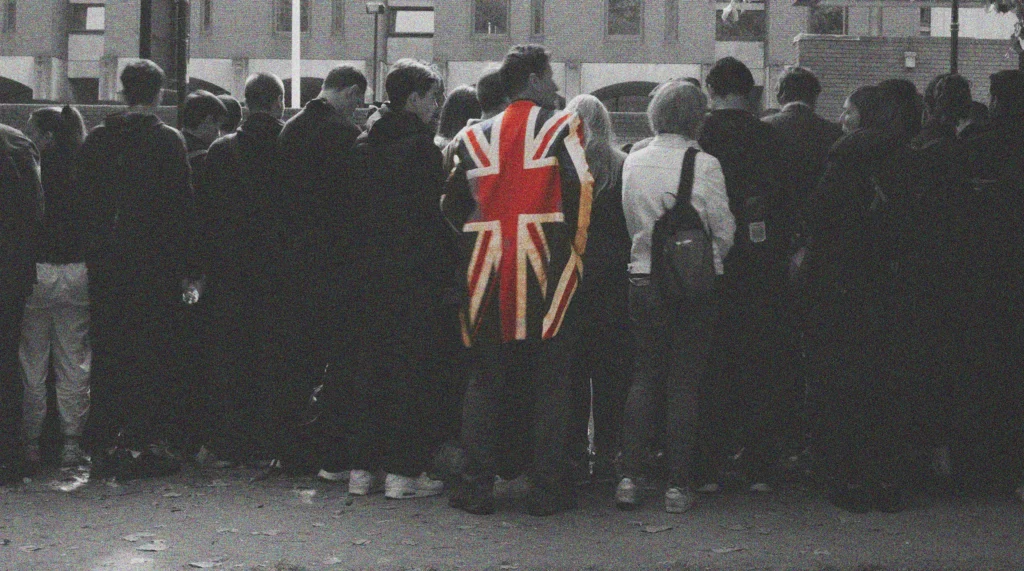 Image of a crowd in black and white with one person wearing a union jack coat, shown in colour.